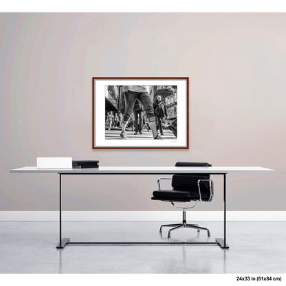 Times Square View Between Legs artwork by Susan Bowen, shown as 24x33 framed print. Features low-angle B&W street photograph of pedestrians mid-stride in Times Square, legs looming large against the city.